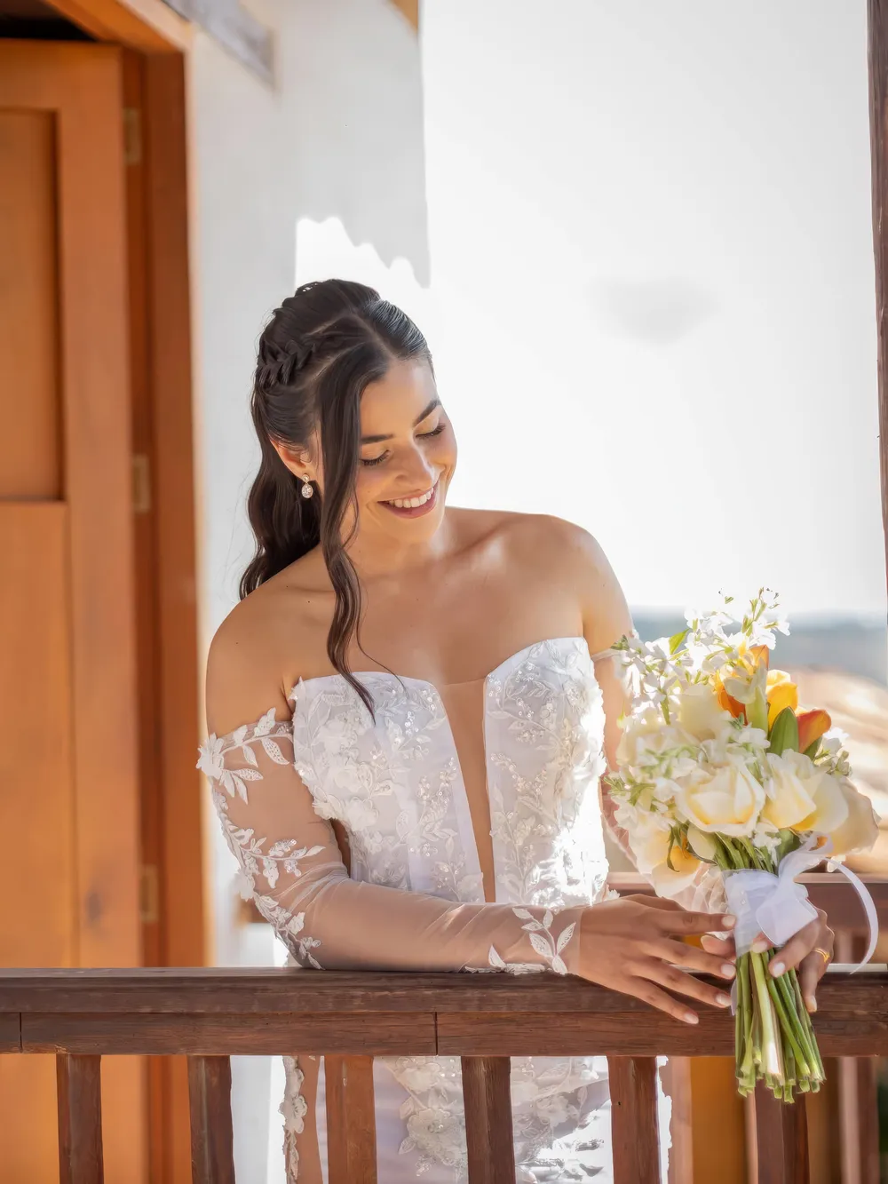 Novia sonriendo apoyada en una baranda de madera con su ramo de flores